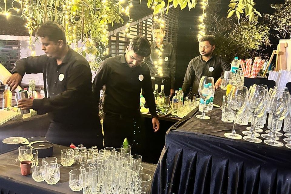Bartenders serving drinks at an outdoor evening event under hanging string lights